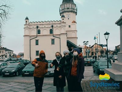 Redaktorzy naczelni z national geographic traveler w towarzystwie naczelniczki wydziału informacji i promocji, przewodniczącej Młodzieżowej Rady Miejskiej - Wiktorii Nowocień oraz Tomasza Jakubowskiego na tle szydłowieckiego ratusza. W prawym dolnym rogu logo: Szydłowiec do zobaczenia!