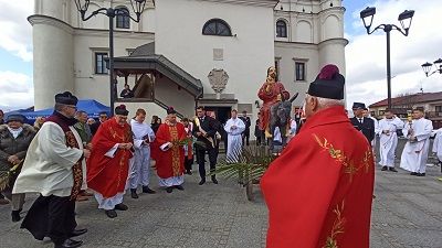 Zdjęcie z Niedzieli Palmowej. Na tle szydlowieckiego ratusza ustawiła się delegacja: Burmistrsz Szydłowca, Zastępca Burmistrza, Radni Miejscy i Powiatowi i Starosta szydłowiecki. Obok stoją księża i ministranci z św. Zygmunta w Szydłowcu i Osiołek Palmowy.